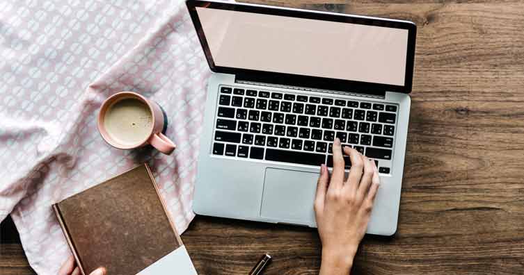 woman's hand at laptop with coffee and a book